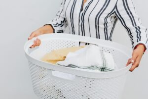 A close-up of a woman holding a white laundry basket filled with fresh, clean clothes.
